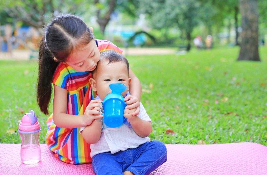 Older sister helping a younger sibling to drink from a sippy cup