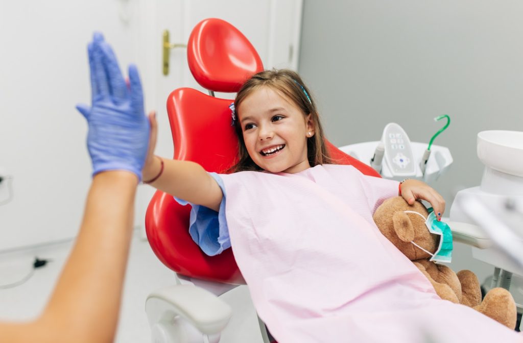 Smiling girl sitting in red dentist chair and giving dentist a high five