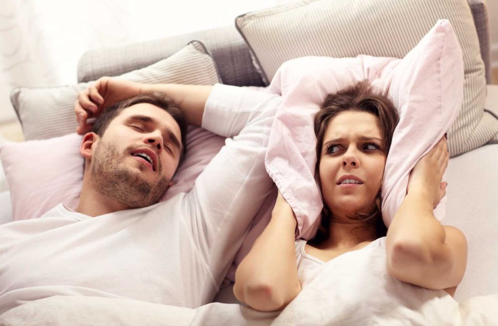 married couple struggling with husband's sleep apnea on white sheets with warm filtered lighting