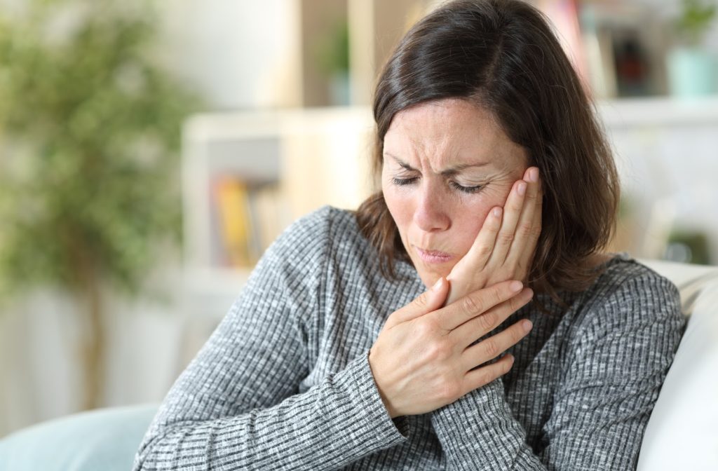 Woman sitting on chair as she experiences toothache while touching her face.