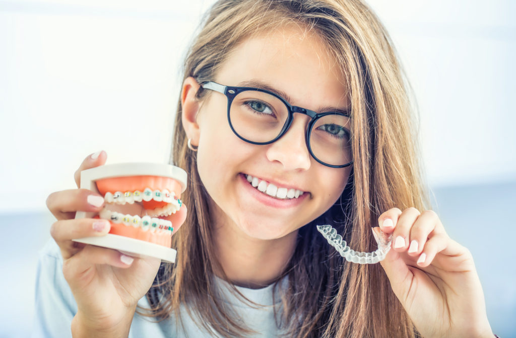 Young girl holding teeth model with braces on and Invisalign on the other hand.