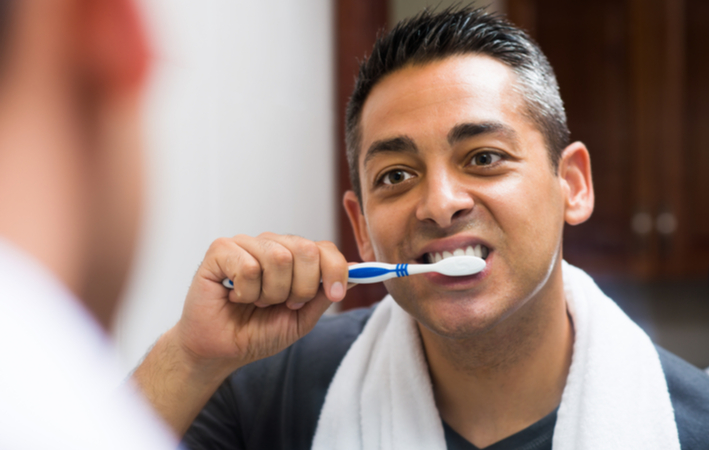 Man smiling in mirror to brush teeth while looking in mirror