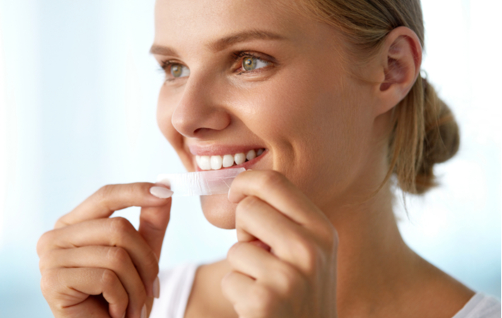 Young smiling women applying whitening strips to enhance appearance of teeth