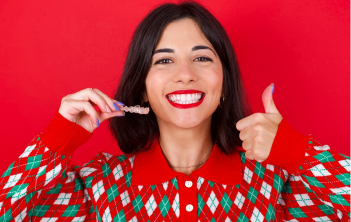 Happy smiling women giving thumbs up while holding teeth whitening tray in other hand