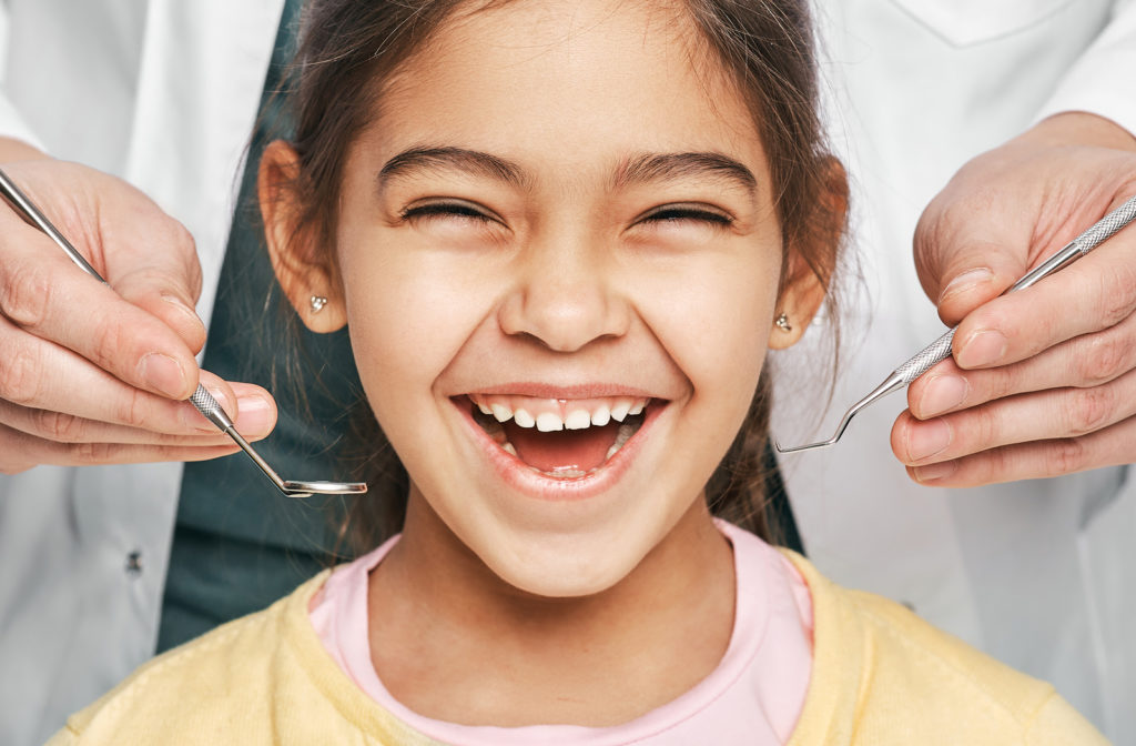 Smiling girl with dentist in background with dental tools ready to operate on patients mouth