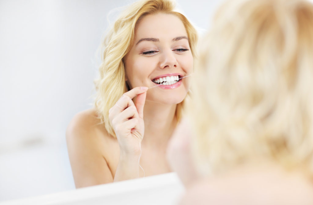 Happy women looking in mirror at self while flossing her teeth