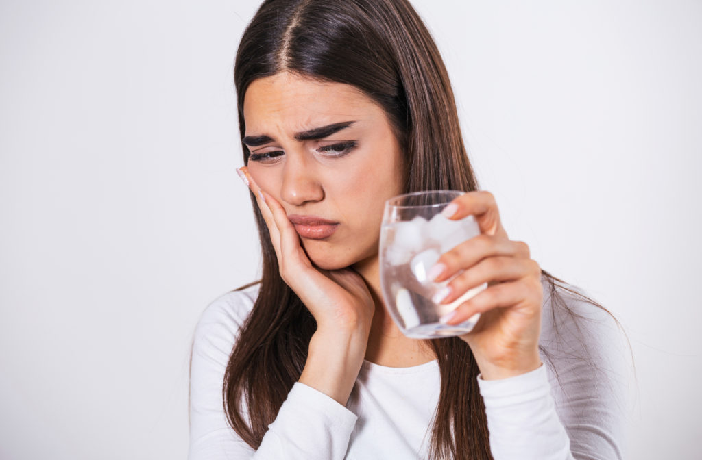 Women experiencing toothache due to temperature sensitivity while drinking water with ice