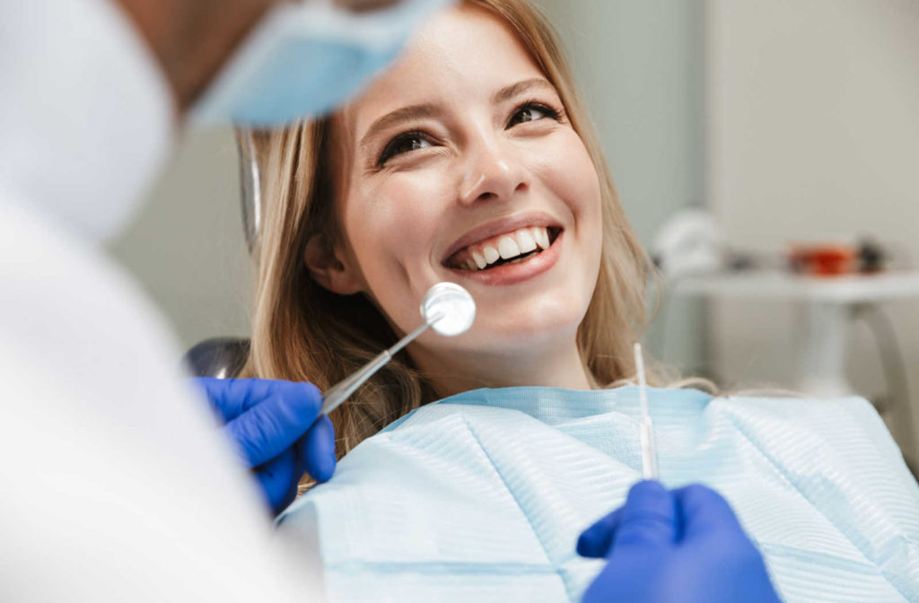 A female dental patient smiling at a dentist who is holding dental tools.