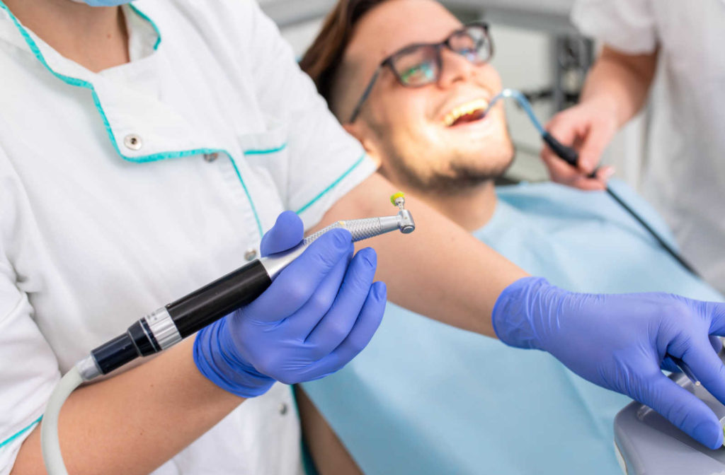 A dentist holding a polishnig tool with a patient smiling in the background.