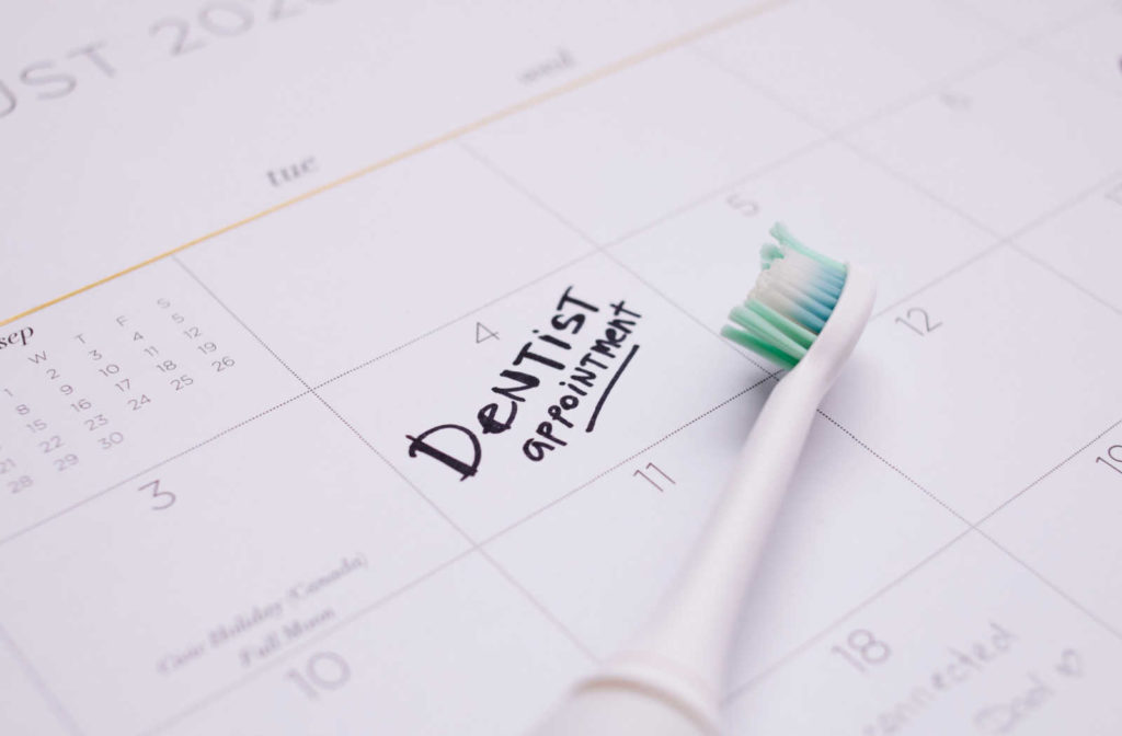 The words "dentist appointment" written in black on a calendar with a toothbrush laying next to it.