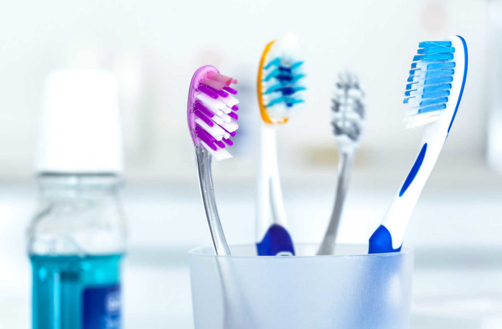 Four toothbrushes sitting upright in a cup with mouthwash in the background.