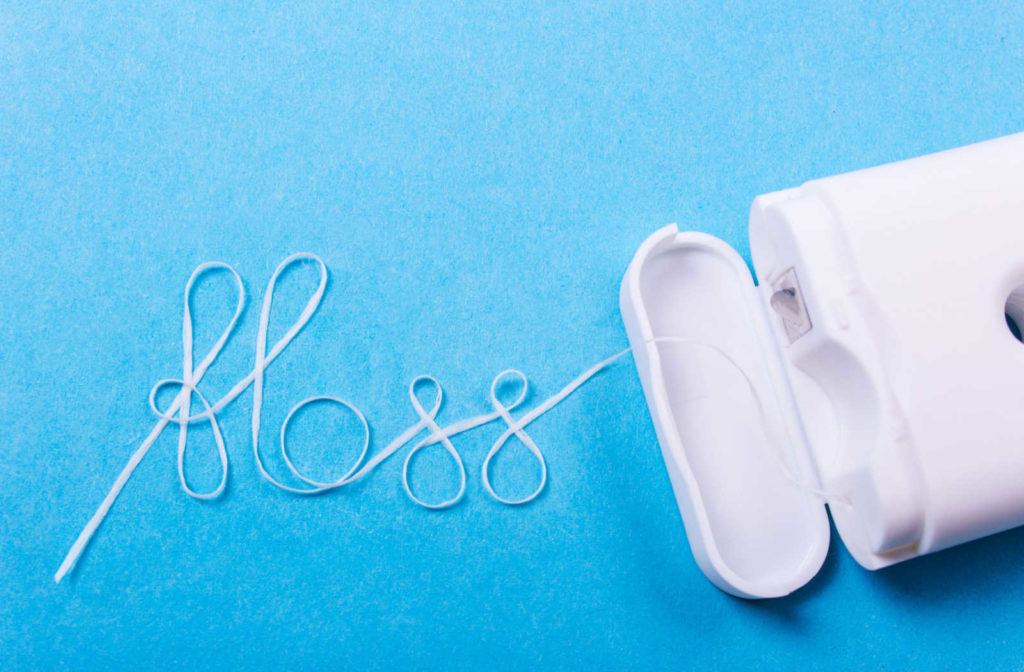 Floss pulled out of it's container and arranged to spell the word floss in cursive writing.