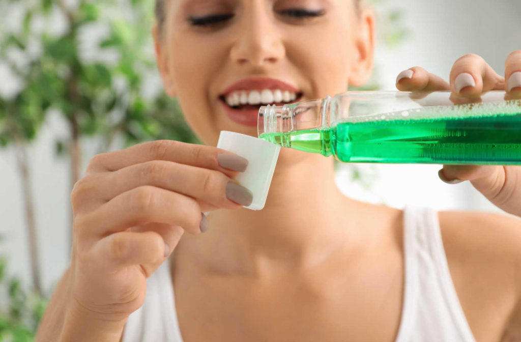A woman smiling while pouring mouthwash into the cap to rinse her mouth and help maintain good oral hygiene.