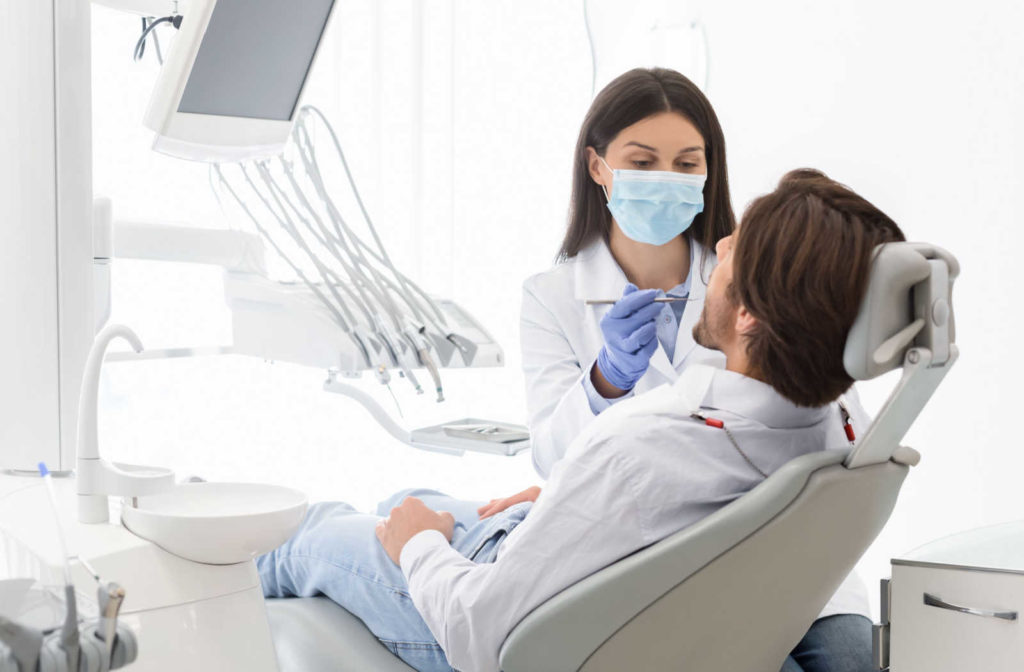 A female dentist is examining the teeth of a male patient that is lying in the dental chair. The dentist can tell the patient is smoking due to the stain on his teeth.