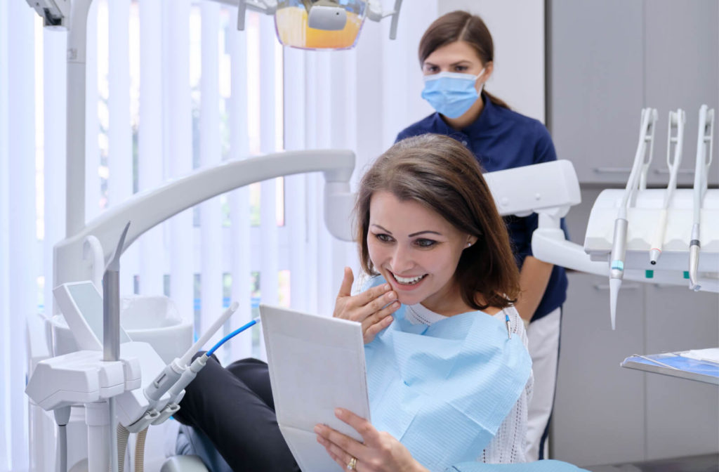 Patient on a dental chair checking her teeth in a mirror after cleaning done by a dentist