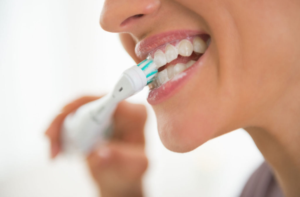 A close-up of a woman showing the proper positioning of brushing her teeth with an electric toothbrush.