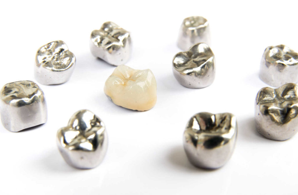 Different kinds of dental crowns like metal and porcelain crowns placed on a white surface.