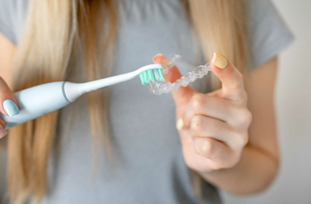 A woman holding a clear aligner on her left hand and cleaning it with a toothbrush on her right hand.