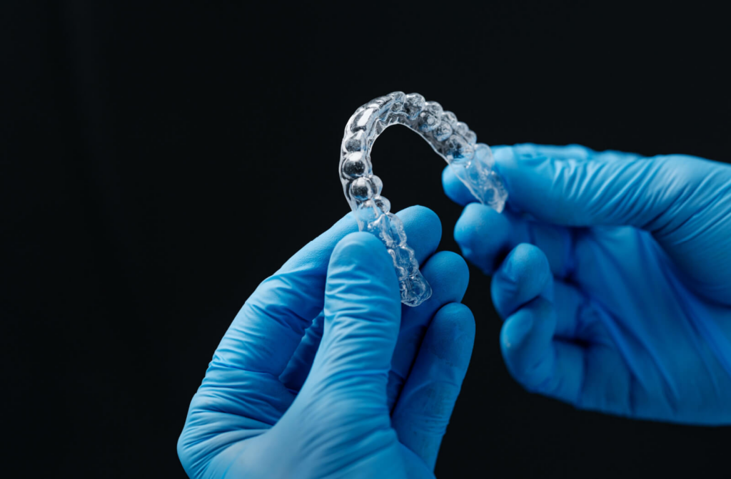 A close-up of a dentist's gloved hands holding a clear aligner used in invisible orthodontic treatment.
