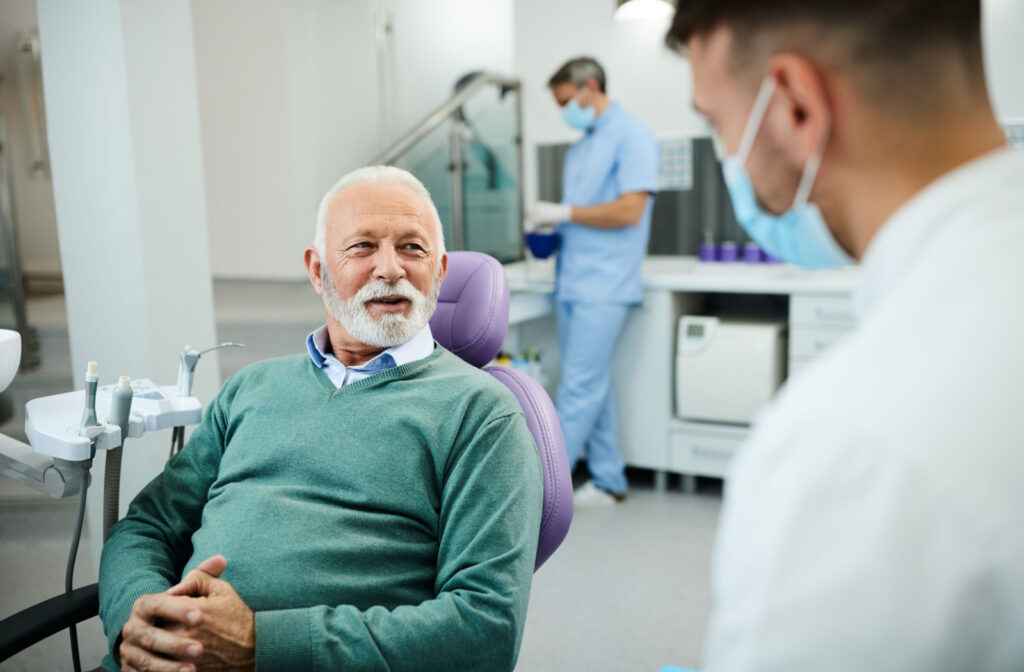 A senior man sitting in a dental office and talking to his male dentist.