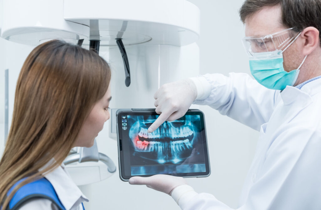 A dentist explaining a dental procedure to a woman while holding a tablet with dental X-ray image.
