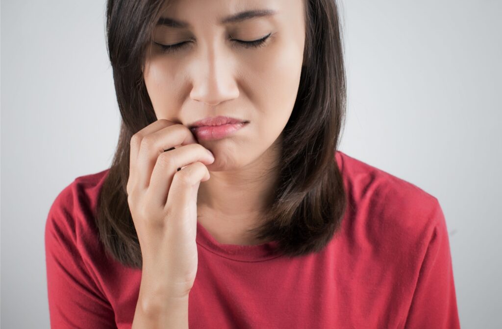 A woman with close eyes experiencing itchy gums and scratching it from the outside of her mouth.