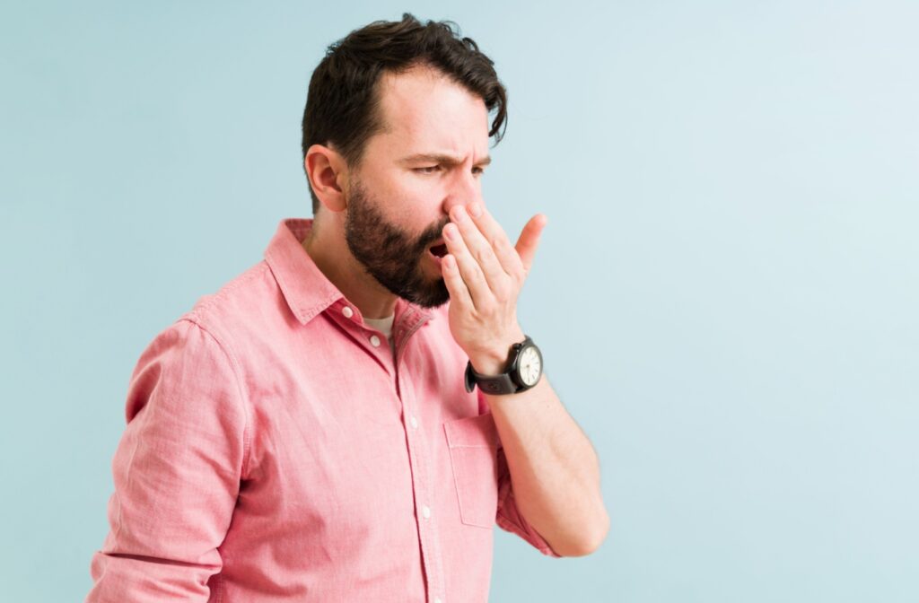 A man in a pink shirt breathing in to his palm to check if his breath smells.
