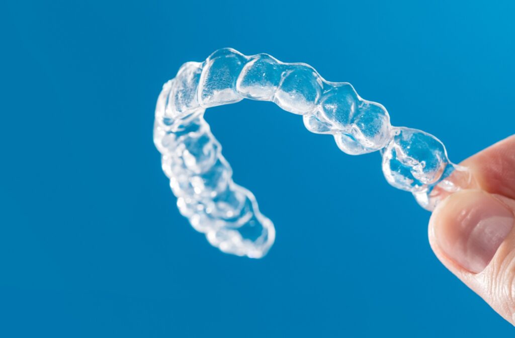 A close-up of a hand holding a clear Invisalign aligner against a blue background.