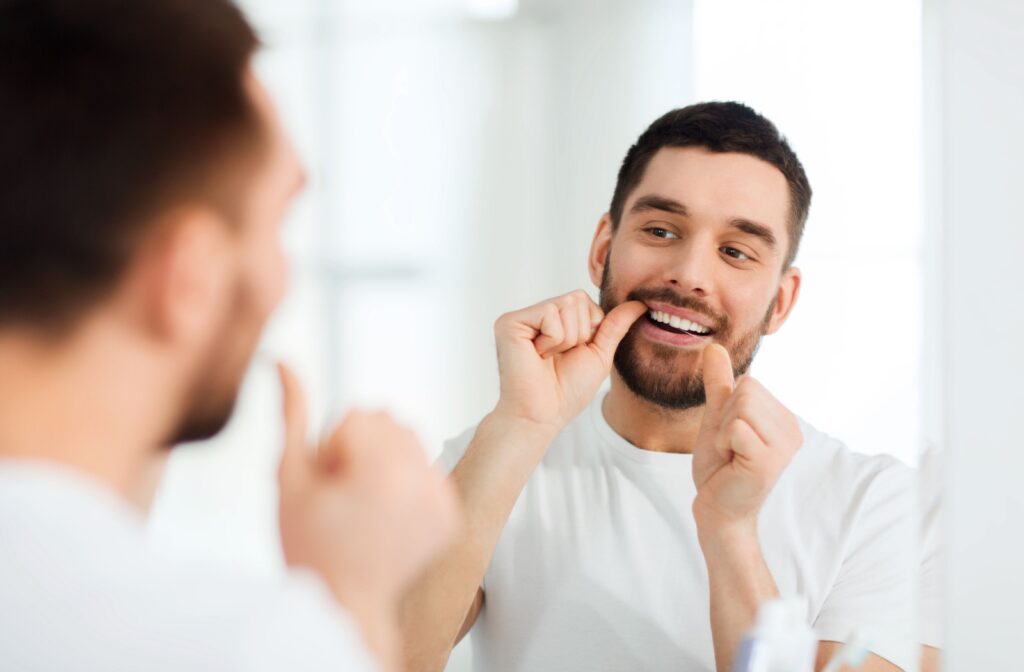 A young man smiling and looking in the mirror while flossing.