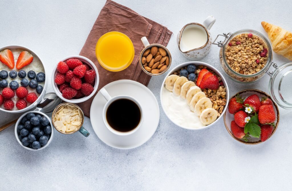 Flatlay of a breakfast spread on a table with black coffee, orange juice, berries, nuts, and granola