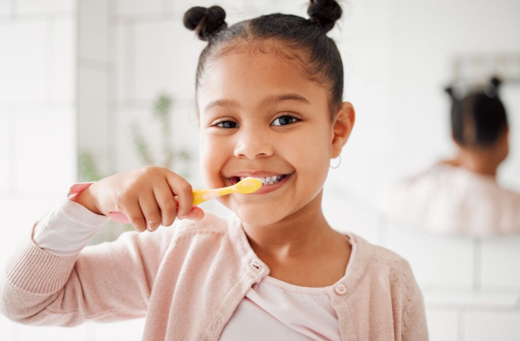 Young girl happily brushing her teeth in a bright, white bathroom.