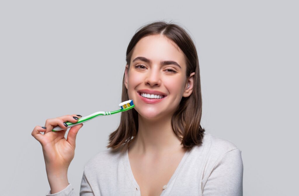 a patient smiles while holding a toothbrush, practicing healthy oral hygiene to prevent tartar buildup.