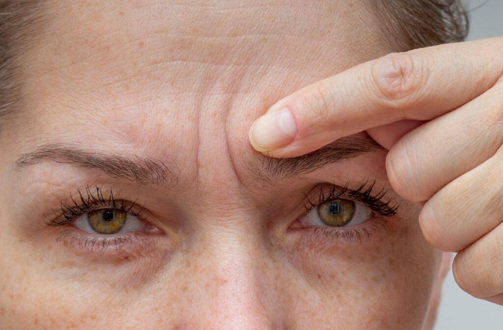 A close-up of a patient, pointing to their forehead, concerned about their wrinkles