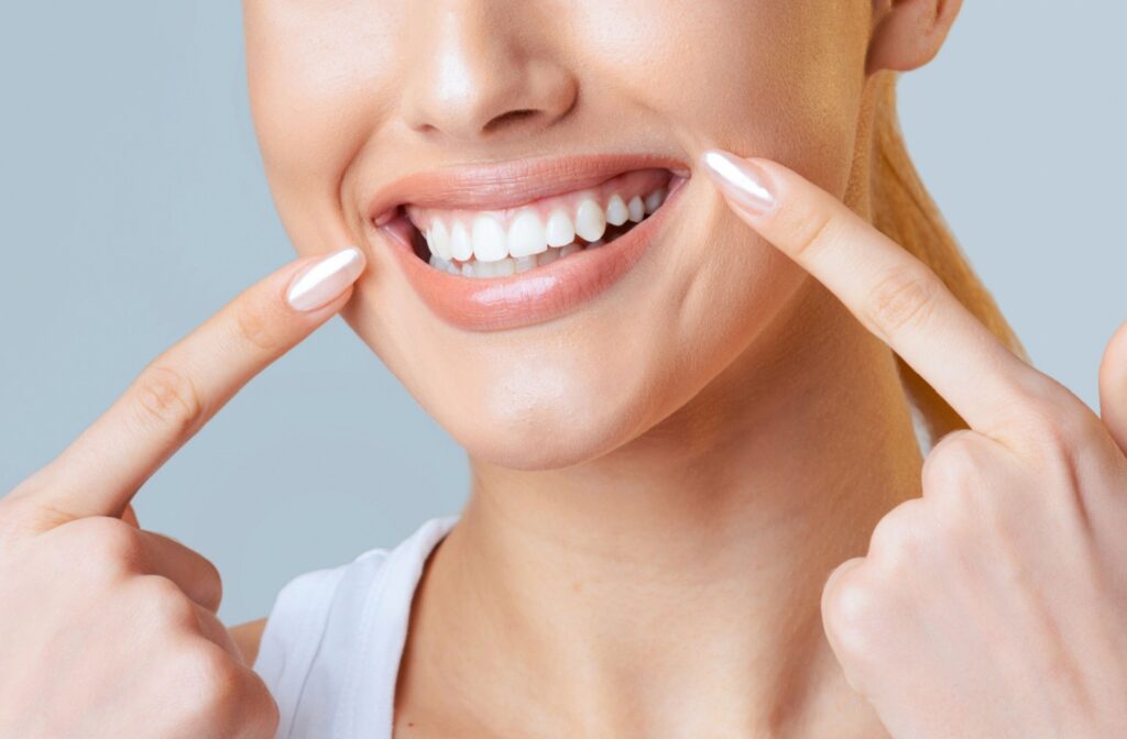 A close-up of a smiling patient pointing at their white teeth after receiving a professional teeth whitening.