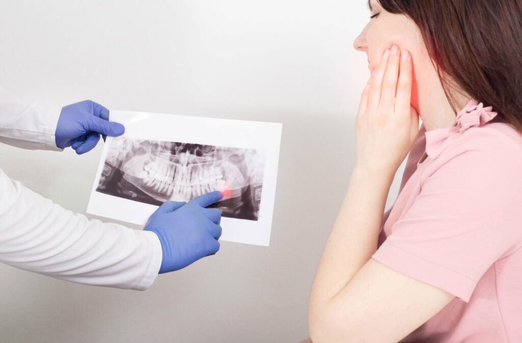 A person holding their jaw while their dentist shows them an X-ray with their impacted wisdom tooth on it